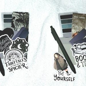 Peut inclure: Deux ensembles de papeterie comprenant des stylos noirs, des marque-pages et des autocollants. Le premier ensemble inclut des autocollants avec le texte "Obstinate Headstrong Girl" et "Still into fairytales but now they're spicier". Le second pr&eacute;sente un autocollant "Be Yourself".