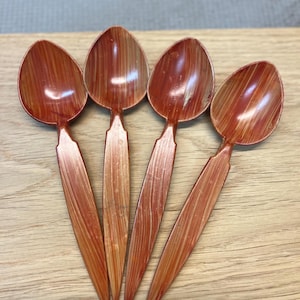 Puede incluir: Cuatro cucharas de color marrón rojizo con un patrón de vetas de madera están dispuestas sobre una superficie de madera de color claro. Las cucharas tienen un cuenco en forma de lágrima y un mango largo y delgado. Las cucharas son de material brillante.