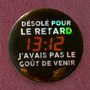May include: A black and gold button with the text "Désolé pour le retard 13:12 J'avais pas le goût de venir" in white.