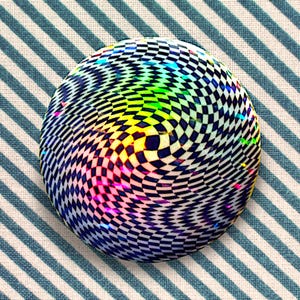 Puede incluir: Un botón redondo, de cuadros negros y blancos con un patrón de espiral de arcoíris. El botón tiene un acabado brillante.
