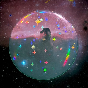 Peut inclure: Un autocollant rond transparent avec une finition holographique. L'autocollant présente un motif de galaxie avec des étoiles et une nébuleuse en arrière-plan. L'autocollant est parfait pour ajouter une touche d'éclat à tout projet.