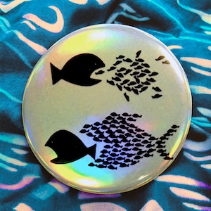 Puede incluir: Una pegatina redonda e iridiscente con un diseño en blanco y negro de dos peces. El pez más grande se está comiendo una escuela de peces más pequeños. El pez más pequeño está siendo comido por una escuela de peces más pequeños.