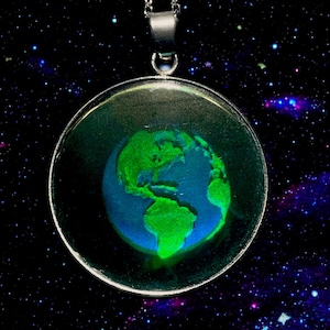Peut inclure: Un collier avec un pendentif en argent en forme de globe terrestre en verre rond, représentant une image verte et bleue de la Terre. Le pendentif est placé sur un fond noir avec une galaxie d'étoiles.