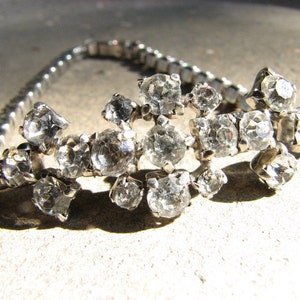 May include: A silver chain bracelet with a cluster of clear rhinestones in a floral design.