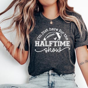 May include: A gray t-shirt with a white graphic that says "I'm just here for the halftime show" with a football and heart design.