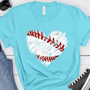Puede incluir: Una camiseta azul turquesa con un gr&aacute;fico de b&eacute;isbol en forma de coraz&oacute;n blanco. El b&eacute;isbol tiene costuras rojas.