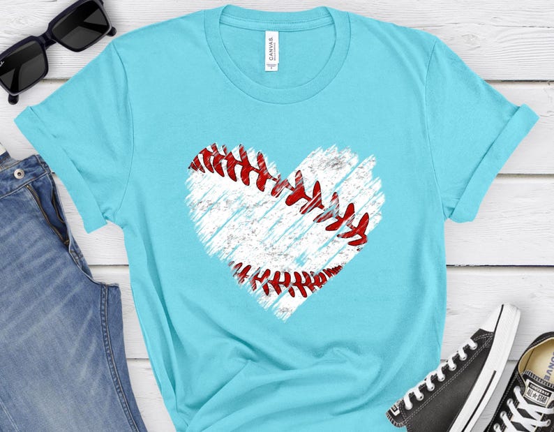 Puede incluir: Una camiseta azul turquesa con un gr&aacute;fico de b&eacute;isbol en forma de coraz&oacute;n blanco. El b&eacute;isbol tiene costuras rojas.