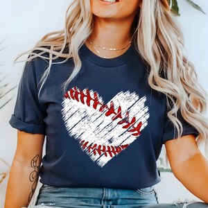 Puede incluir: Una camiseta azul marino con un gr&aacute;fico de b&eacute;isbol blanco en forma de coraz&oacute;n. El b&eacute;isbol tiene costuras rojas.