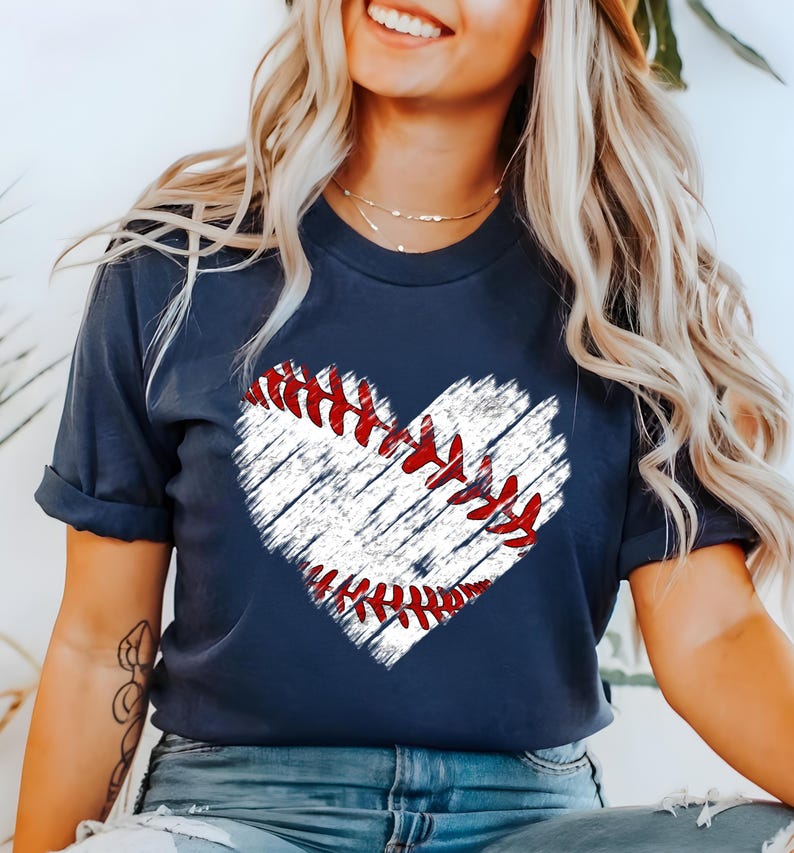 Puede incluir: Una camiseta azul marino con un gr&aacute;fico de b&eacute;isbol blanco en forma de coraz&oacute;n. El b&eacute;isbol tiene costuras rojas.