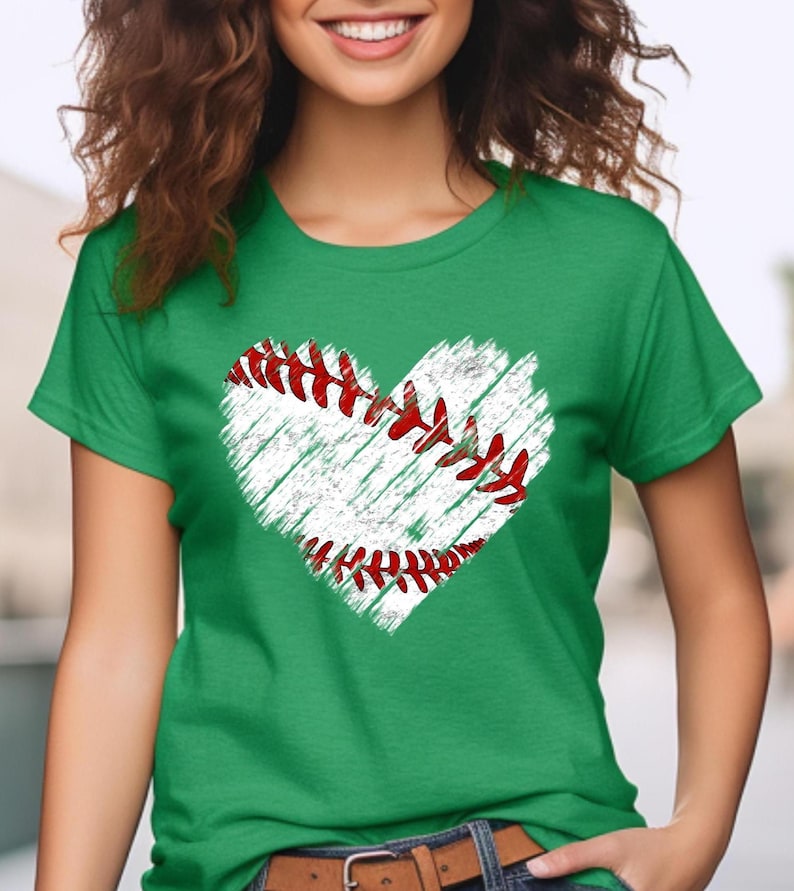 Puede incluir: Una camiseta verde con un gr&aacute;fico de b&eacute;isbol blanco en forma de coraz&oacute;n. El b&eacute;isbol tiene costuras rojas.