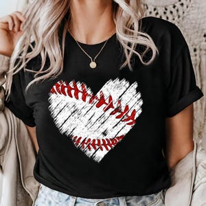 Puede incluir: Camiseta negra con un gr&aacute;fico de b&eacute;isbol en forma de coraz&oacute;n blanco. El coraz&oacute;n tiene costuras rojas y un aspecto desgastado.
