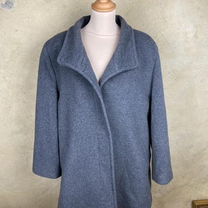 May include: A grey wool coat with a wide collar and three-quarter sleeves. The coat is displayed on a mannequin. The coat has a simple, classic design, suitable for various occasions. The coat is a solid colour.