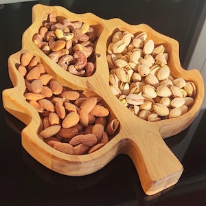Könnte beinhalten: Ein Holztablett in Form eines Baumes mit drei separaten Fächern. Die Fächer sind mit Mandeln, Cashewnüssen und Pistazien gefüllt.