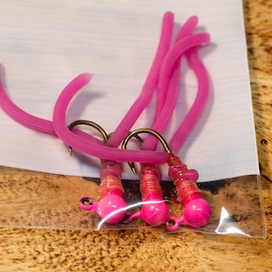 May include: Four pink fishing lures with hooks and a pink bead on each lure. The lures are packaged in a clear plastic bag.