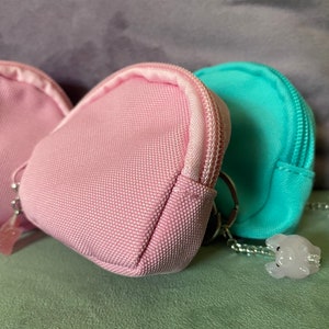 May include: Two pink and one turquoise fabric coin purses with zipper closures and silver keychains with small white charms attached.