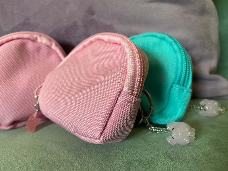 May include: Two pink and one turquoise fabric coin purses with zipper closures and silver keychains with small white charms attached.