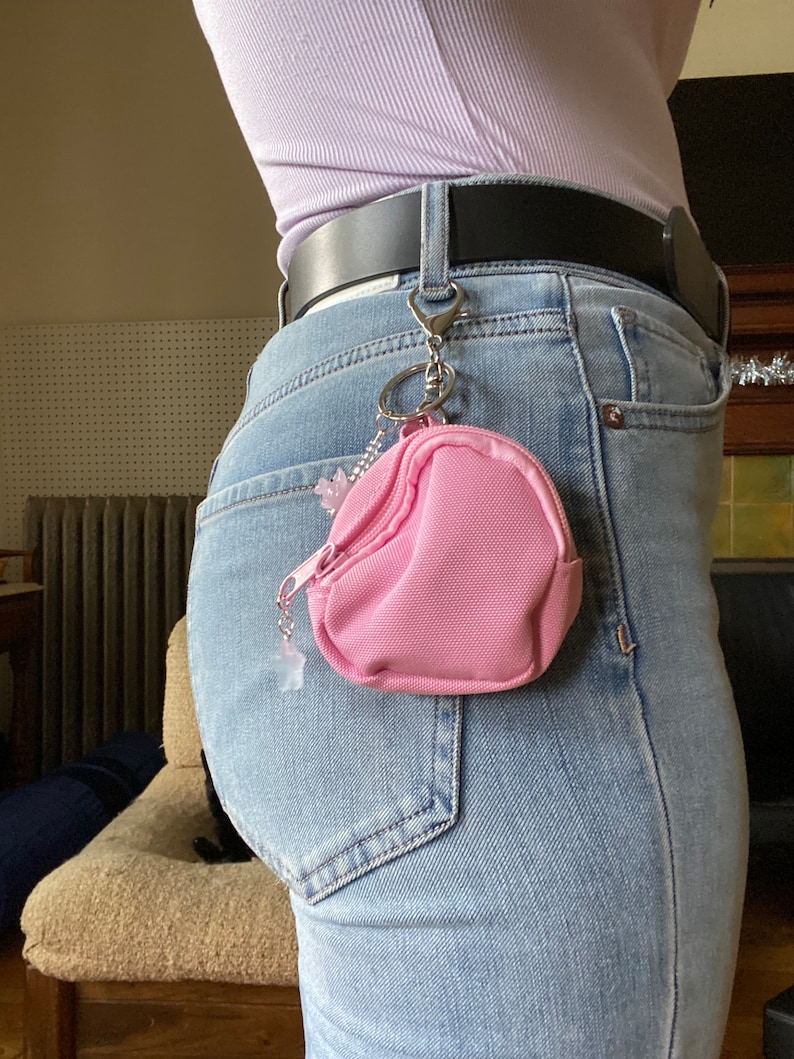 May include: A pink zippered pouch with a silver chain attached to a belt loop. The pouch is hanging from the belt loop of a pair of blue jeans.