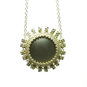 以下が含まれることがあります： 小さなビーズで作られた丸いペンダントが付いたゴールドネックレス。ペンダントは円形で、濃いグレーの中心部があります。