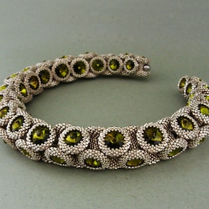Könnte beinhalten: Ein silbernes und grünes Perlenarmband mit einer Reihe runder, facettierter grüner Perlen.
