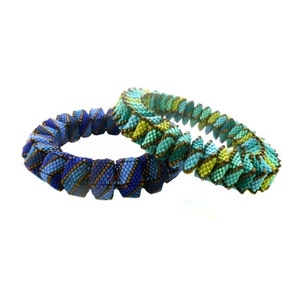 May include: Two beaded bracelets, one blue and gold, the other green and gold, are coiled together. The bracelets are made of small, square beads.
