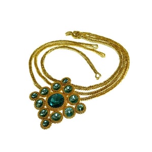 以下が含まれることがあります： 大きな緑色の宝石のペンダントが付いた金のチェーンネックレス。ペンダントは、花の形に配置された小さな緑色の宝石で作られています。