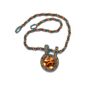 May include: A beaded necklace with a pendant featuring a large, round, orange gemstone surrounded by smaller beads in shades of green and orange.
