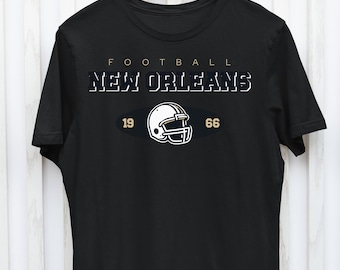 May include: Black t-shirt with the text "FOOTBALL NEW ORLEANS" in white and gold lettering. A white football helmet with a gold facemask is centered below the text with the numbers "19" and "66" on either side.