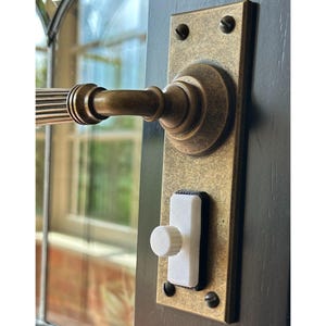 May include: A white door knob with a black trim, mounted on a brass door handle with a decorative backplate.