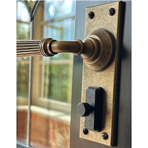 May include: A brass door handle with a lever design and a black latch. The handle has a textured finish and is mounted on a wooden door.