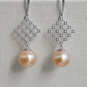 May include: A pair of silver earrings with a delicate geometric design and a single, round, peach-colored pearl dangling from each.