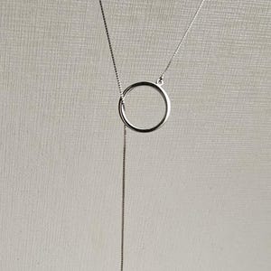 Puede incluir: Un collar de cadena de plata con un colgante circular y una sola perla colgando de la parte inferior.