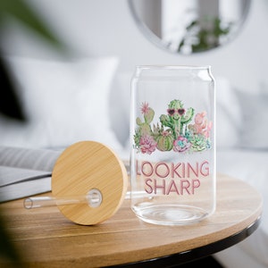 Peut inclure: Une canette en verre transparent avec un couvercle en bambou et une paille. La canette est décorée d'un motif de cactus avec le texte "LOOKING SHARP" imprimé dessus.