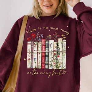 Op de afbeelding: Bordeaux sweatshirt met een afbeelding van boeken met bloemen. De tekst op de trui luidt: "Er zijn niet te veel boeken."