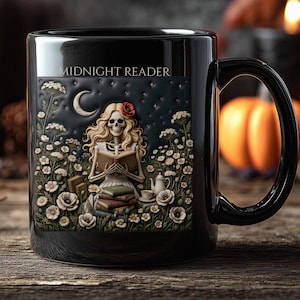 Op de afbeelding: Een zwarte keramische mok met de tekst MIDNIGHT READER boven een gedetailleerde illustratie van een skelet met lang blond haar dat een boek leest te midden van een veld met witte bloemen, een maansikkel, een theepot en een stapel boeken.