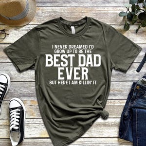 May include: A green t-shirt with white text that reads "I never dreamed I'd grow up to be the best dad ever but here I am killin' it".