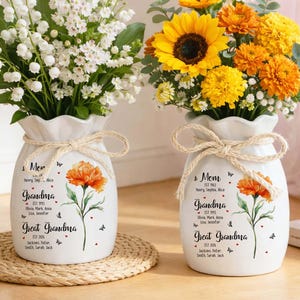 May include: Two white ceramic vases with floral arrangements. One vase holds white flowers, the other yellow and orange flowers. Each vase has a floral design and text that reads "Mom", "Grandma", and "Great Grandma".