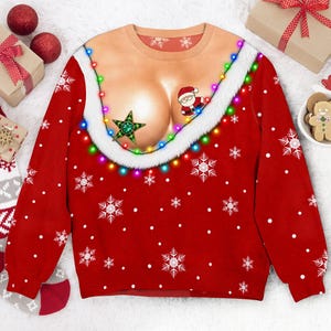 Puede incluir: Una sudadera roja de manga larga con un estampado gráfico de un pecho color carne adornado con un borde de piel sintética blanca, una cadena de luces navideñas de colores, una estrella verde y una pequeña figura de Papá Noel sobre copos de nieve.