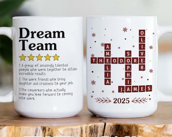 May include: White ceramic mug with the words "Dream Team" in black. The front of the mug has a definition of "Dream Team" and the back has a crossword puzzle with names and the year 2025. The mug has a handle.