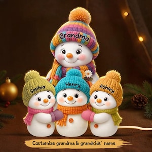 Può includere: Statuine di pupazzi di neve con cappelli e sciarpe di lana colorati. Il pupazzo di neve più grande ha la parola "Grandma" sul cappello. I pupazzi di neve più piccoli hanno i nomi "Sophia", "Henry" e "Ashley". Il testo in basso dice "Customize grandma & grandkids' name".