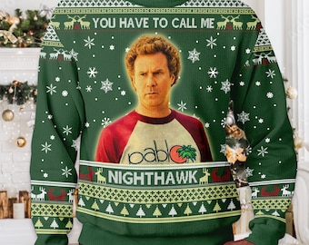 May include: A dark green long-sleeve sweater featuring a graphic of a man wearing a white and red baseball shirt with the text 'pablo' and a palm tree. The sweater includes the text 'YOU HAVE TO CALL ME NIGHTHAWK' and white snowflake patterns.