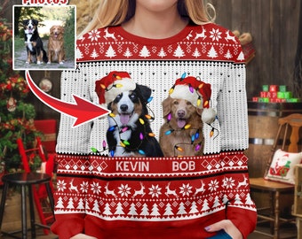 May include: A red and white Christmas sweater featuring two dogs wearing Santa hats and string lights. The sweater has the names "KEVIN" and "BOB" below the dogs, and the text "CUSTOM your PHOTOS" is at the top.