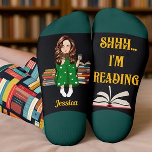May include: Black socks with a green cuff and toe. One sock features a cartoon of a person reading with the name "Jessica". The other sock says "SHHH... I'M READING" with an open book graphic.