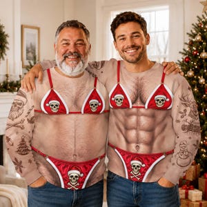 Puede incluir: Una sudadera beige de manga larga con un estampado realista de un torso musculoso con vello, luciendo un bikini rojo con gráficos de calaveras y gorros de Papá Noel. Las mangas muestran dibujos lineales negros de calaveras y copos de nieve.