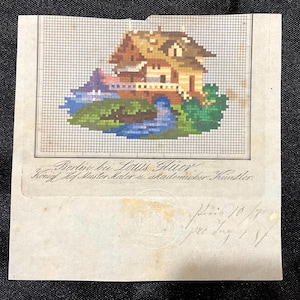 May include: A vintage cross-stitch pattern featuring a detailed house with a bridge over a blue river, surrounded by green foliage. The pattern is on a grid, with text below and handwritten notes. The image is on aged paper.