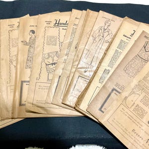 May include: A collection of vintage sewing pattern booklets, featuring illustrations of clothing designs. The covers are aged with a tan hue, and the text is in German. The booklets are stacked, with some covers displaying dates like "Januar 1938" and "September 1939".