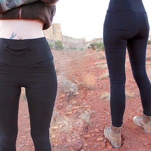 May include: Two women wearing black leggings with a high waist. The leggings have a decorative rope detail at the waist. The women are standing in a desert landscape.