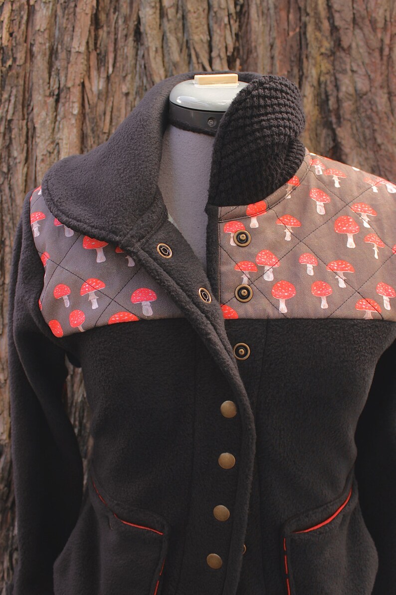 May include: A black fleece jacket with a brown and red mushroom print on the front. The jacket has a high collar and a zipper closure. It has a quilted design and a red trim around the pockets.