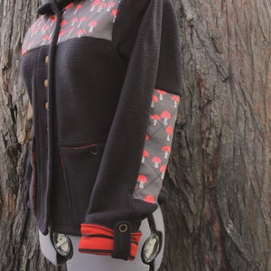 May include: A black fleece jacket with a red and white mushroom pattern on the chest and sleeve. The jacket has a hood and a zipper closure.