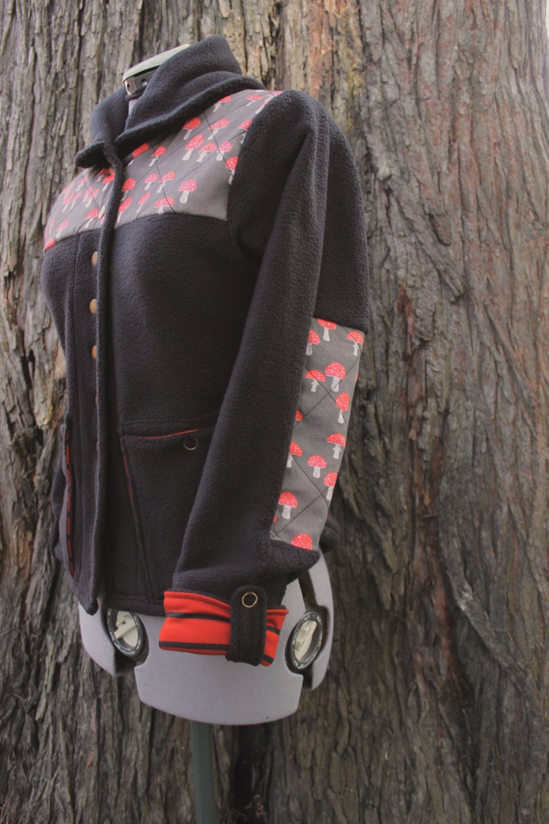 May include: A black fleece jacket with a red and white mushroom pattern on the chest and sleeve. The jacket has a hood and a zipper closure.