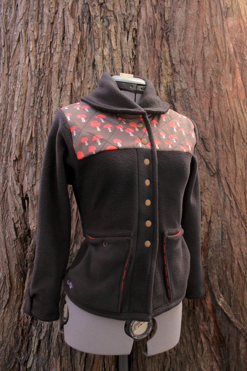 May include: A black fleece jacket with a red and brown mushroom print on the front. The jacket has a collar, a button closure, and two pockets.